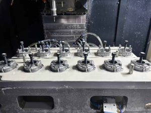 12 die casting metal parts clamped in a CNC machining fixture, industrial manufacturing setup with machining tool overhead