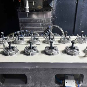 12 die casting metal parts clamped in a CNC machining fixture, industrial manufacturing setup with machining tool overhead